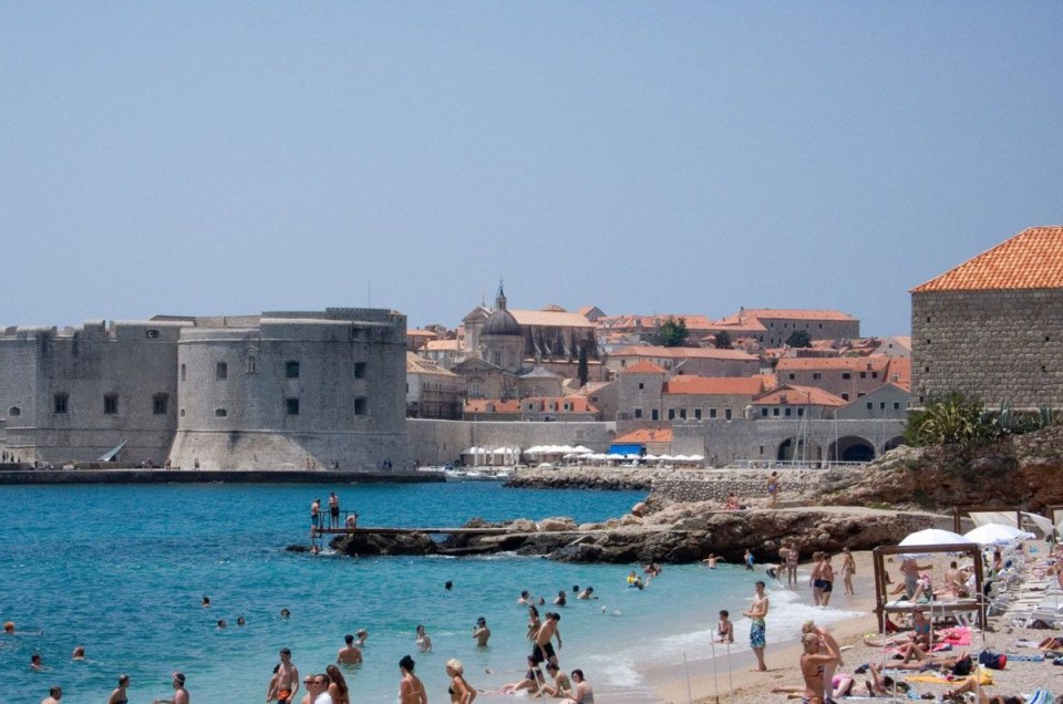Beachgoers enjoy a sunny day near Dubrovnik's historic city walls and vibrant blue sea.