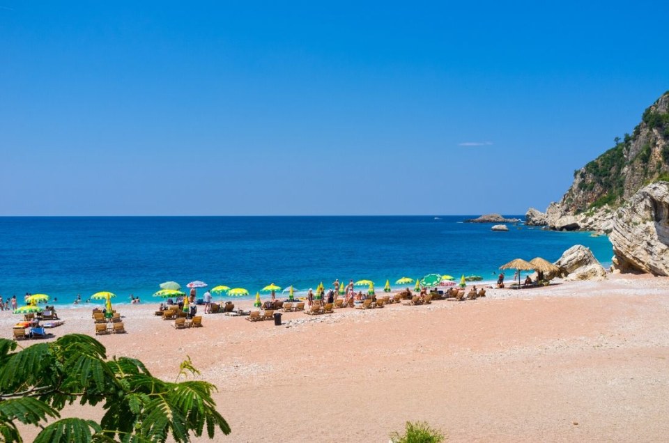 A beach scene with people, umbrellas, and clear blue water.