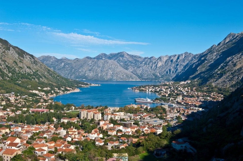 Coastal town surrounded by mountains and a bay under a clear blue sky.